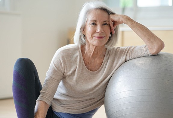 Senior woman smiling while resting against balance ball