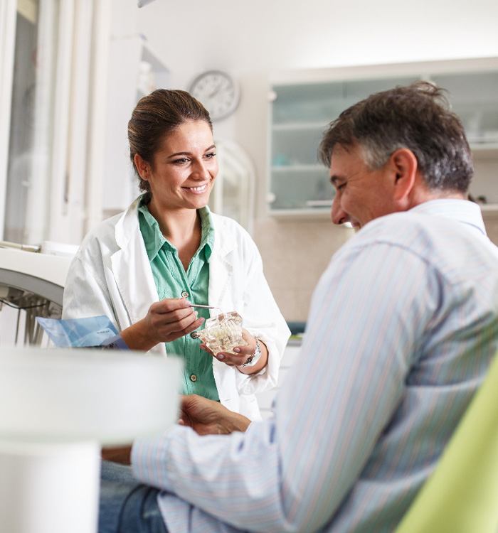 Smiling dentist showing patient model of teeth