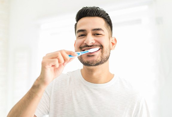 Man smiling while brushing his teeth