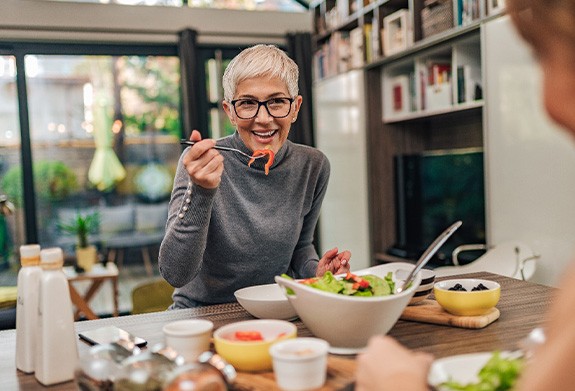 Woman with black glasses smiling while eating with friend