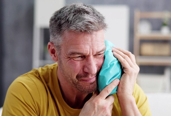 A man holding an ice pack to his face after dental implant surgery