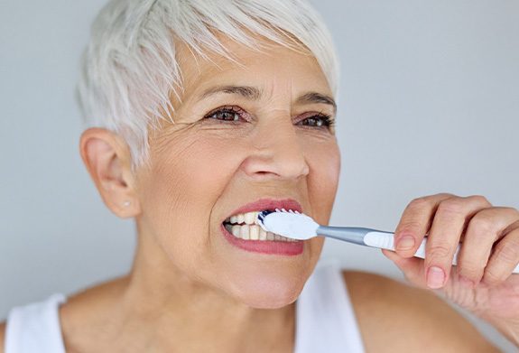 A woman brushing her teeth after dental implant surgery