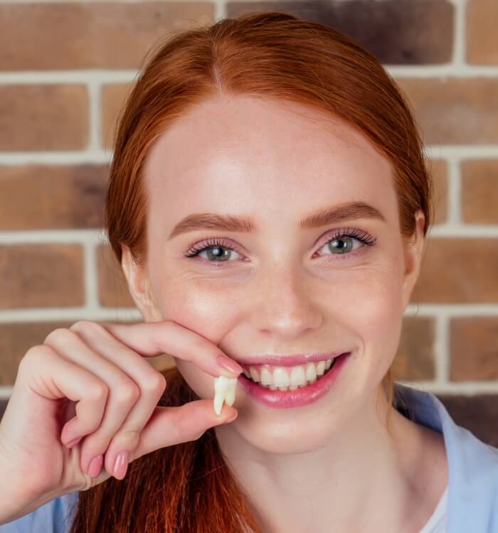 Woman smiling holding a wisdom tooth after extraction