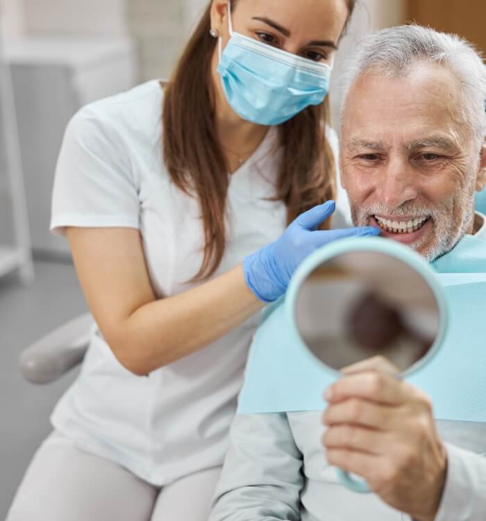 Man looking at smile in mirror after dental implant tooth replacement