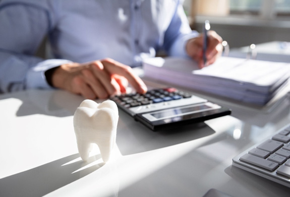 Man pushing buttons on calculator at desk with papers and model tooth
