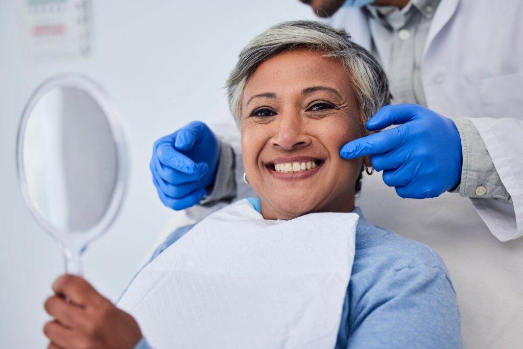 Woman in dental chair holding mirror with dentist pointing to her smile