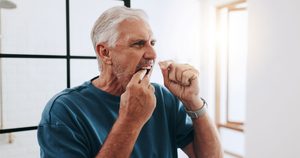 Man with white hair in blue shirt flossing teeth